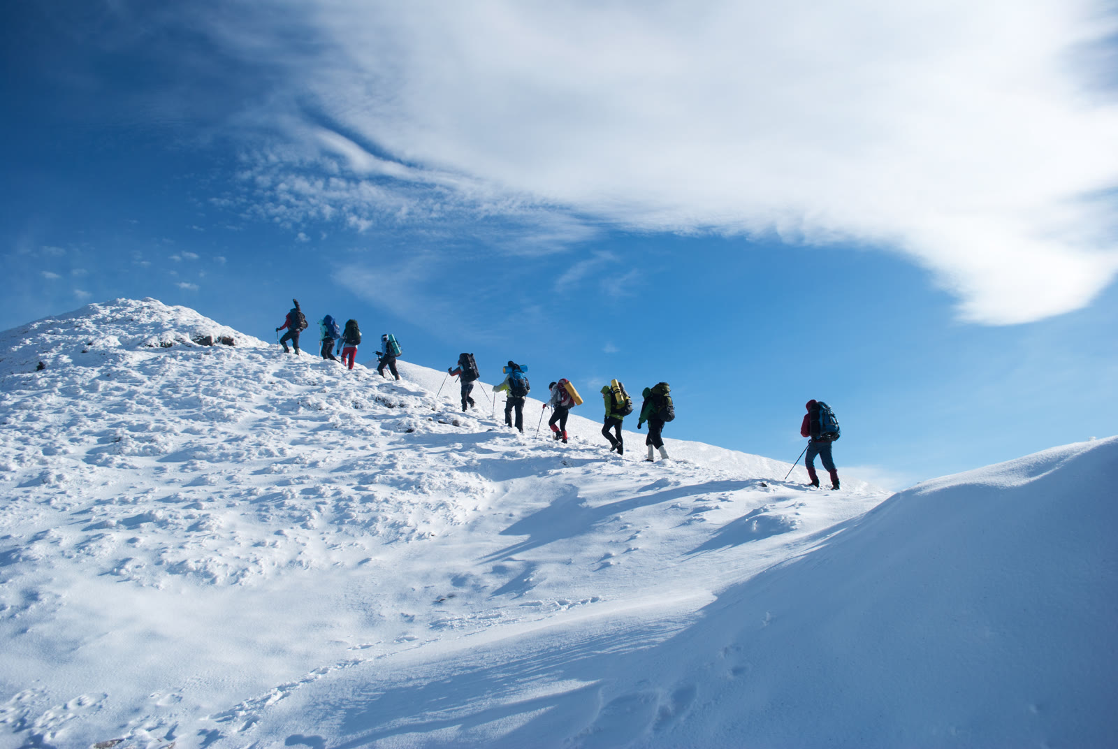 A line of hikers climbing a snow slope together under a blue sky